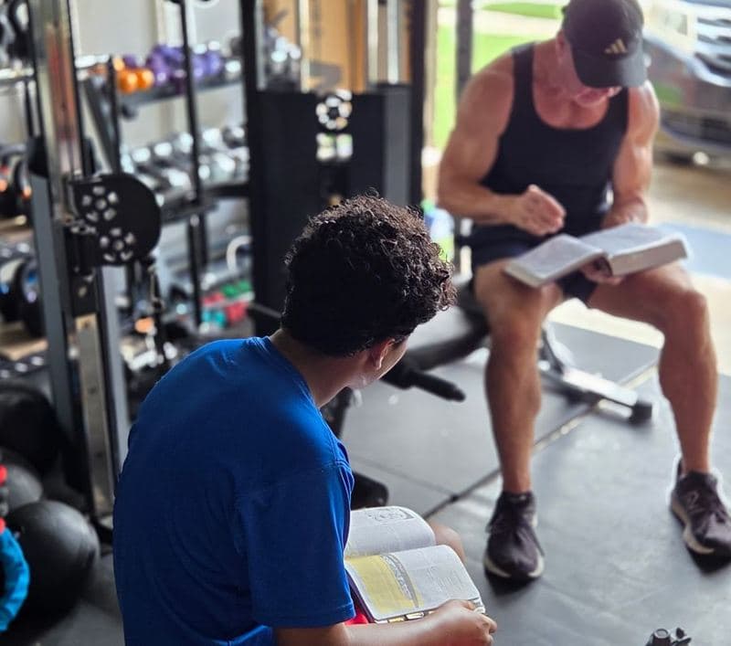 Jeff Mensing and a client sitting with open Bibles in the garage gym