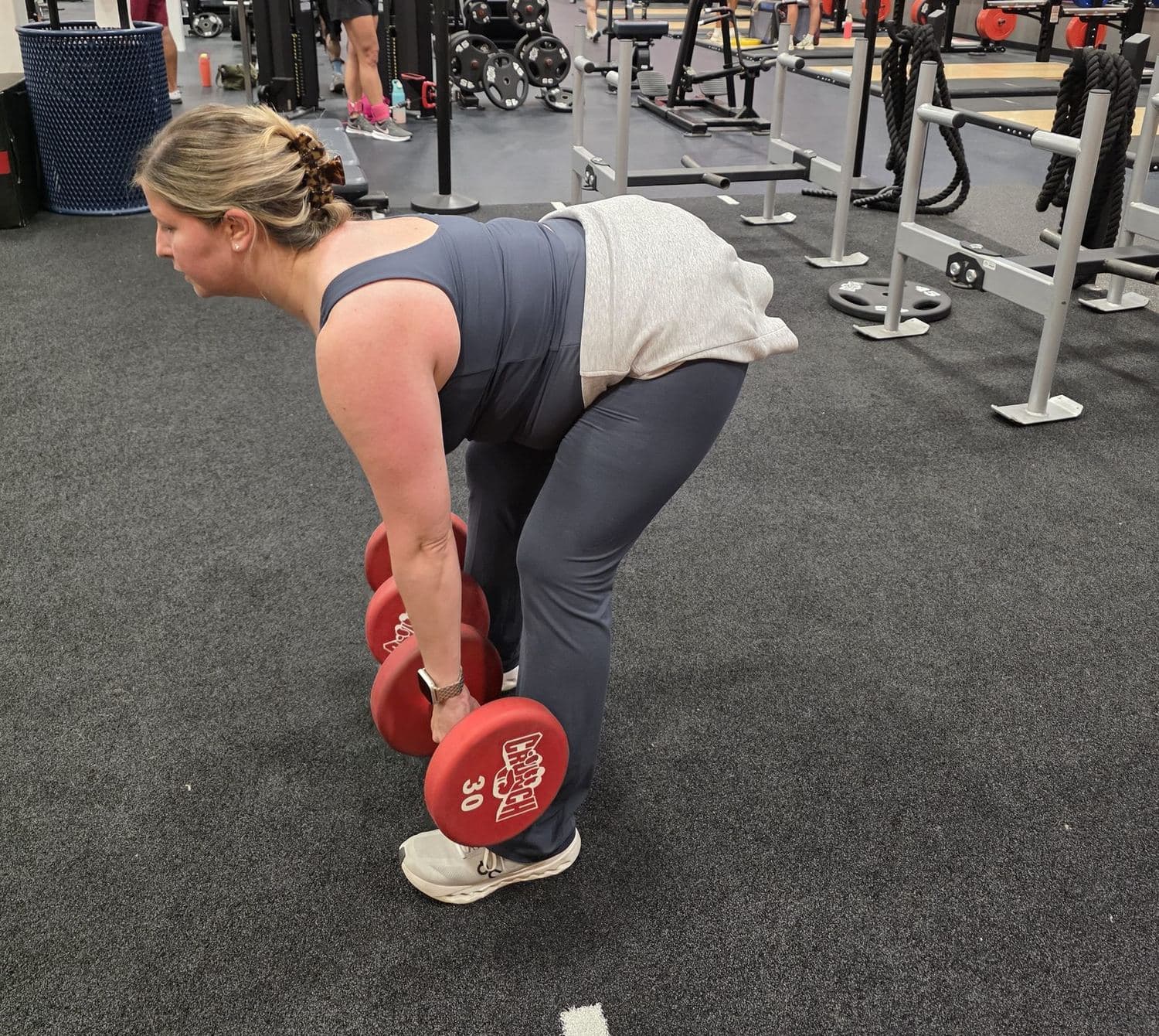 A client lowering a pair of dumbbells through a Romanian deadlift on the gym floor